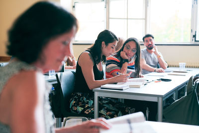 Students discussing over book at desk in classroom