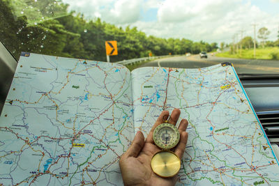 Close-up of person hand holding navigational compass with map by car windshield