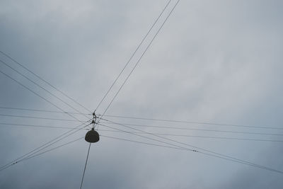 Low angle view of cables and lighting equipment against cloudy sky