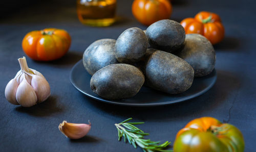 Purple potatoes with tomatoes, garlic, rosemary and olive oil on dark background