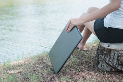 Midsection of woman sitting on grass by lake