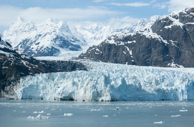 Scenic view of alaskan glacier with snowcapped mountains against sea