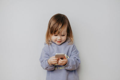 Portrait of young woman using mobile phone against wall