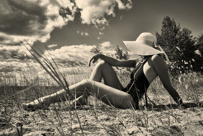 A woman in a swimsuit, hat and sunglasses sunbathes in summer on the riverbank among the grass