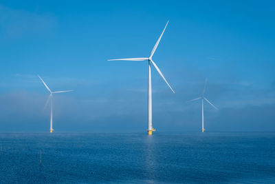 Windmills on field against clear blue sky