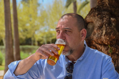 Man drinking beer from glass against trees