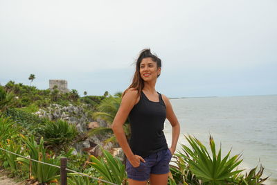 Smiling young woman standing on beach against sky