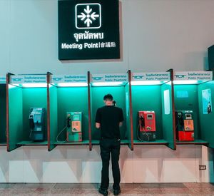 Full length rear view of man standing on public telephone booth 