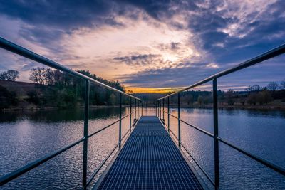 Footbridge over lake against sky during sunset