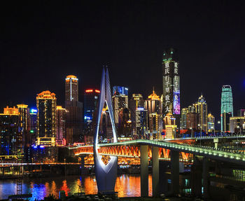 Illuminated bridge over river by buildings against sky at night