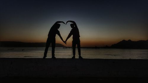 Silhouette couple standing on beach against clear sky during sunset