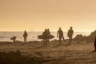 Silhouette people at beach against sky during sunset