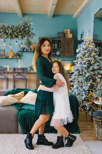 Mother and daughter stand at the christmas tree and hug each other