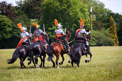 Men riding horses on field against trees