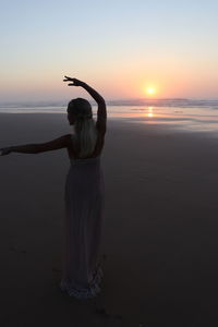 Rear view of woman standing at beach during sunset