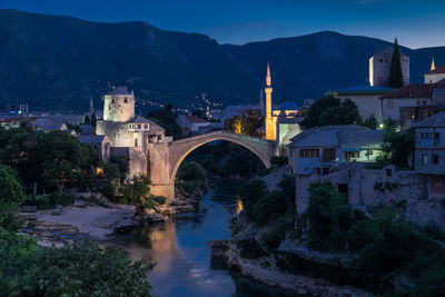 Arch bridge over river by buildings against sky at night