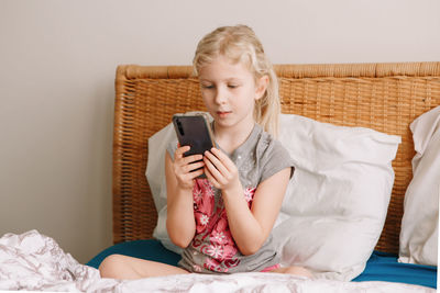 Girl using smart phone while sitting on bed at home
