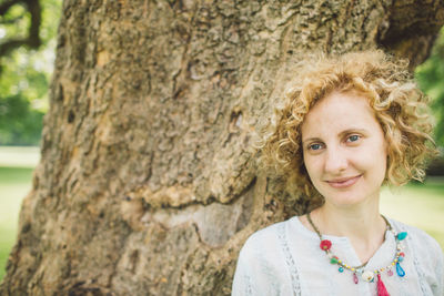 Portrait of smiling woman against tree trunk