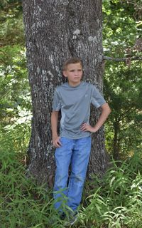 Portrait of boy standing on tree trunk in forest