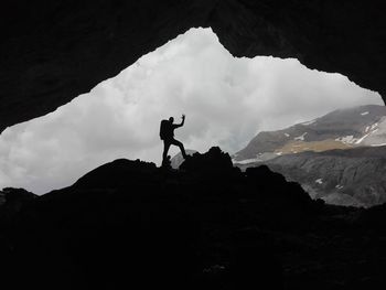 Silhouette man standing in cave against mountains 