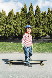 Portrait of confident boy standing with skateboard on footpath at yard