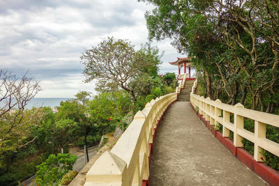 Walkway amidst trees against sky