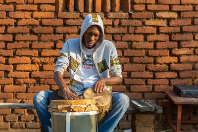 Portrait of smiling young man holding while sitting against brick wall