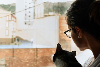 Close-up of woman with cat looking through window at home