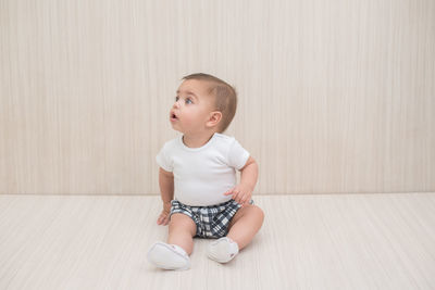 Cute boy looking away while sitting on floor against wall