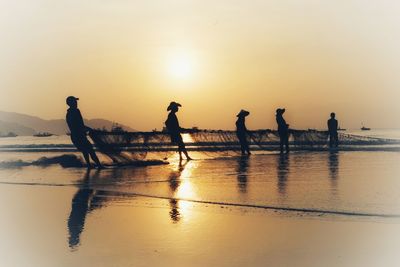 Silhouette people on beach against sky during sunset