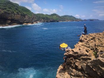 Man standing on rock by sea against blue sky