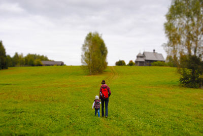 Rear view of woman with baby walking on grassy field