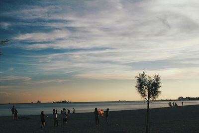 People at beach against sky during sunset