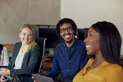 Happy multiracial colleagues sitting together at office