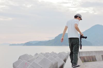 Rear view of young man walking on retaining wall against sky