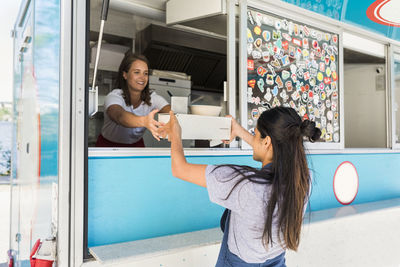 Smiling young multi-ethnic female owner giving container to saleswoman at food truck