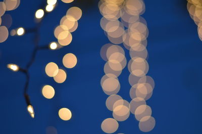 Defocused image of illuminated lights against blue sky