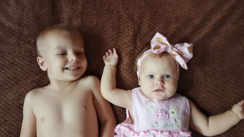 High angle portrait of baby girl with shirtless brother lying on bed