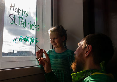 Girl writing on window with father at home