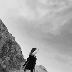 Low angle view of woman standing against cloudy sky