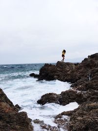 Man standing on cliff by sea against sky