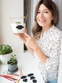 Smiling woman shows handmade decorations for halloween. diy flags and boo sticker on flowerpot.