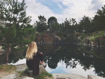 Rear view of woman standing by lake against trees
