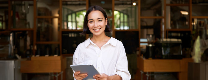 Portrait of young woman using mobile phone while standing in library