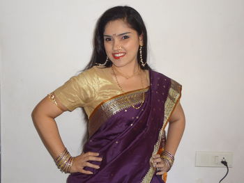 Portrait of smiling woman in sari standing against wall
