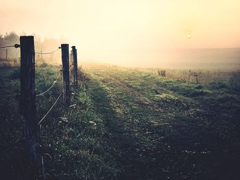 Fence on field against cloudy sky