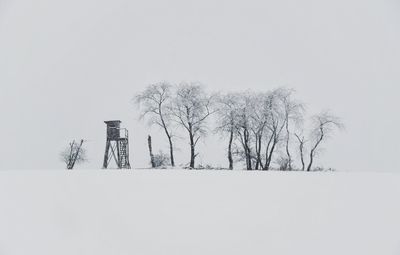 Bare trees on snow field against sky during winter