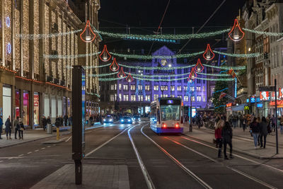 People and tramway on illuminated city street at night