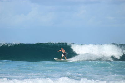 Rear view of young man surfing on sea against sky