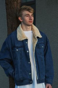 Thoughtful young man looking away while standing against tree trunk